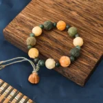Bodhi seed lotus bracelet with moss agate beads overhead view on wooden coaster with braided tassel and carved lotus charm