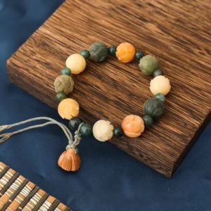Bodhi seed lotus bracelet with moss agate beads overhead view on wooden coaster with braided tassel and carved lotus charm