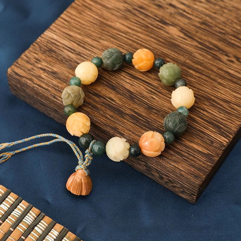 Bodhi seed lotus bracelet with moss agate beads overhead view on wooden coaster with braided tassel and carved lotus charm