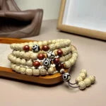 108 Bodhi seed mala beads overhead view showing spotted beige beads with red accent beads and hand-painted Dzi bead pendant on wooden display tray