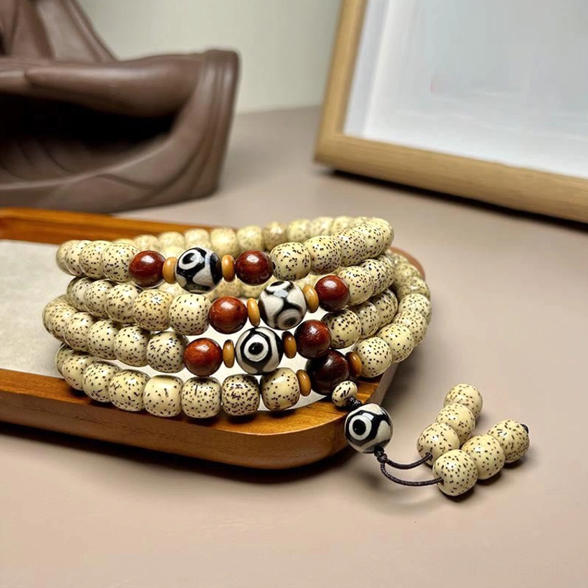 108 Bodhi seed mala beads overhead view showing spotted beige beads with red accent beads and hand-painted Dzi bead pendant on wooden display tray