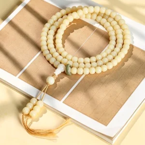 Hand-polished bodhi seed 108 bead mala bracelet with lotus pendant and green jade accent bead, displayed on wooden surface