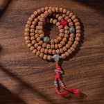 Bodhi seed 108 bead mala with three-eye dzi bead flat lay on wooden surface showing full prayer necklace design