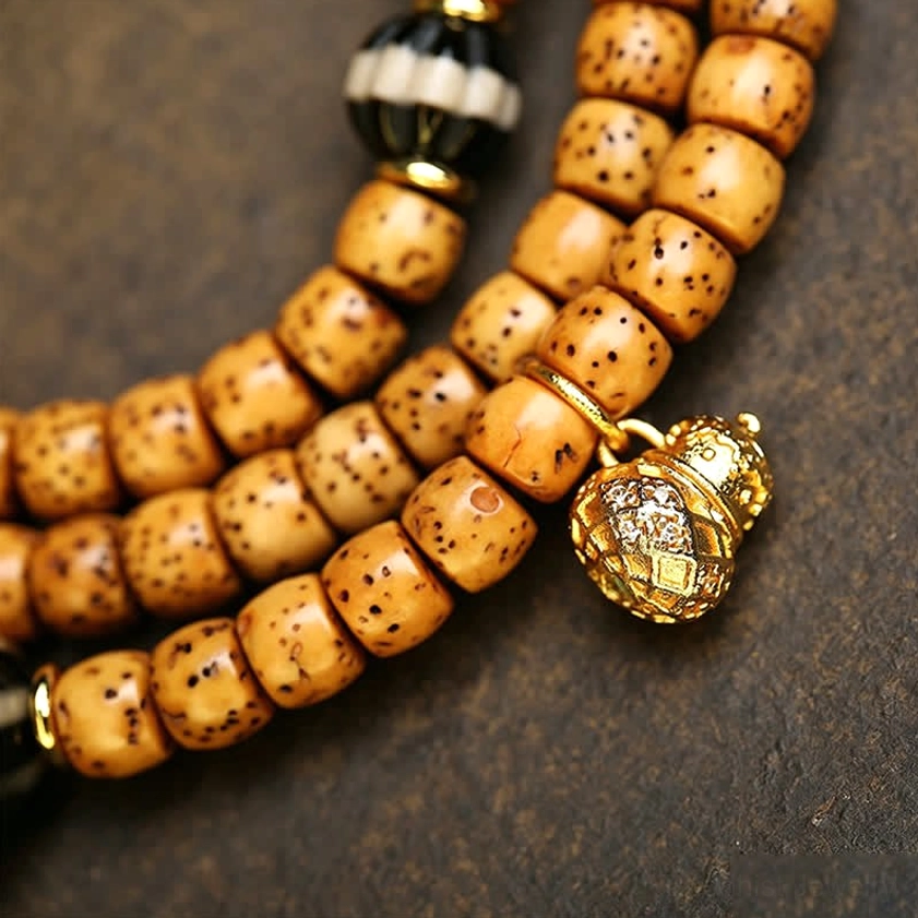 Side view close-up of thick tan spotted Bodhi Seed beads with gold metal prayer charm and striped spacer