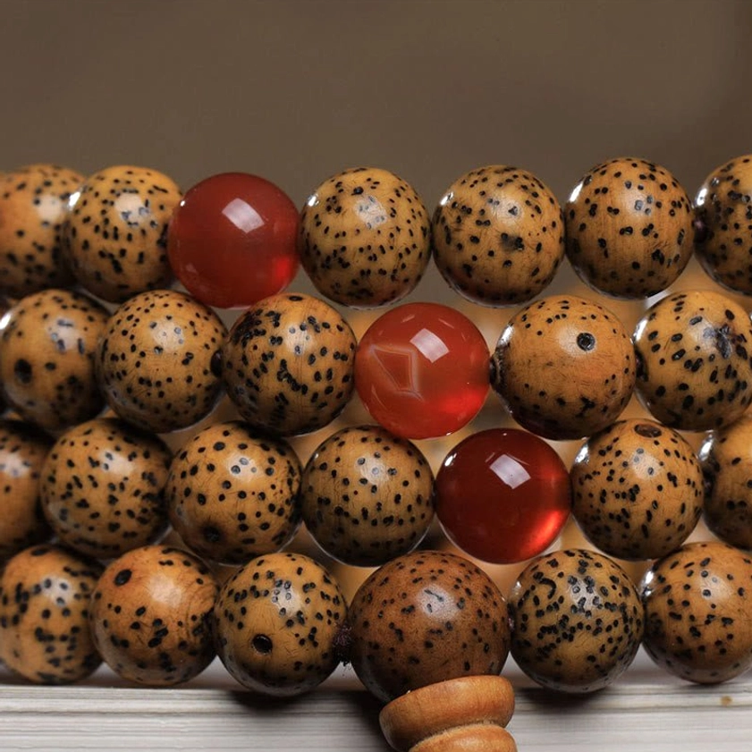 Close-up detail view of bodhi seed mala bracelet featuring large spotted bodhi seeds, multiple red agate spacer beads, and wooden guru bead of Buddhist prayer mala
