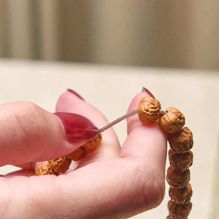 Close-up hands holding Bodhi seed prayer beads showing textured brown seeds with silver thread and red nail polish