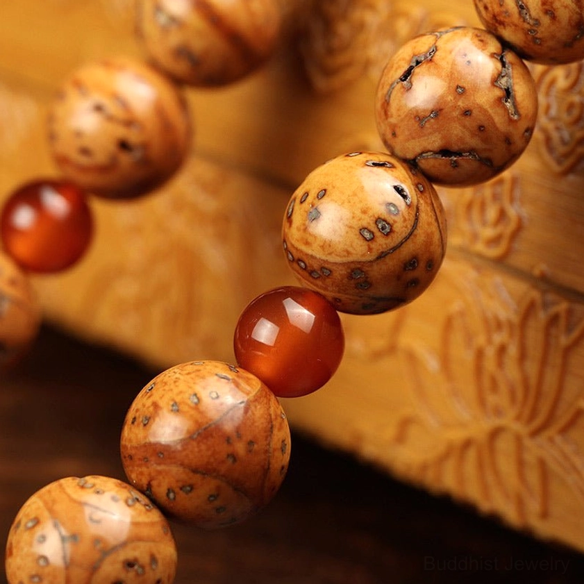 Bodhi seed mala close-up side view with red agate spacers and carved wooden background showing macro bead texture and natural seed pores