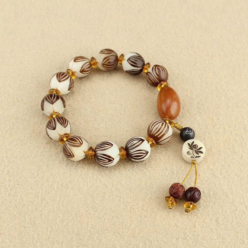 Flat lay view of bodhi seed mala bracelet with mixed carved beads and flower charm tassel pendant on light beige background