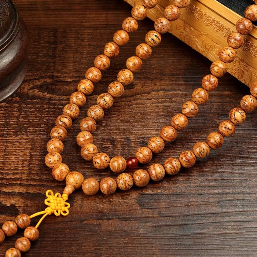 Looped bodhi seed mala bracelet flat lay showing circular strand arrangement with yellow Chinese knot tassel spotted brown seeds on carved wooden table