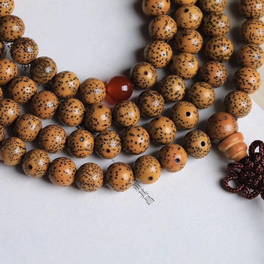 Bodhi seed prayer bracelet side angle close-up on light background, displaying spotted brown bodhi beads, red agate spacer, and braided knot tassel of Buddhist mala