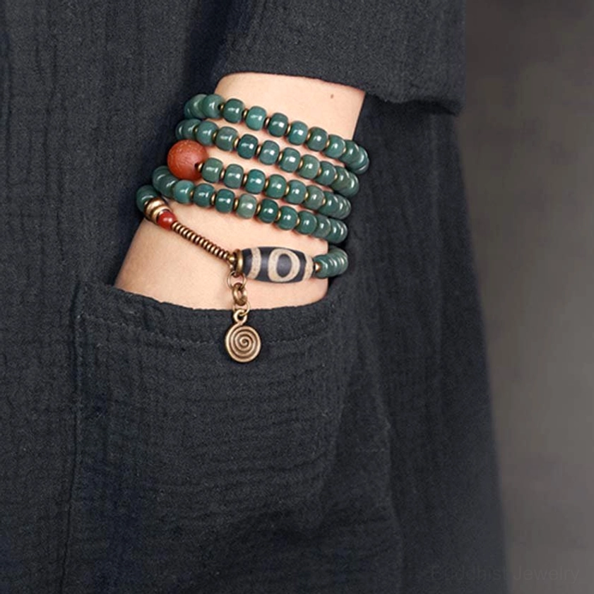 Worn mala bead bracelet on wrist with dzi bead charm hanging accent, styled with dark linen clothing