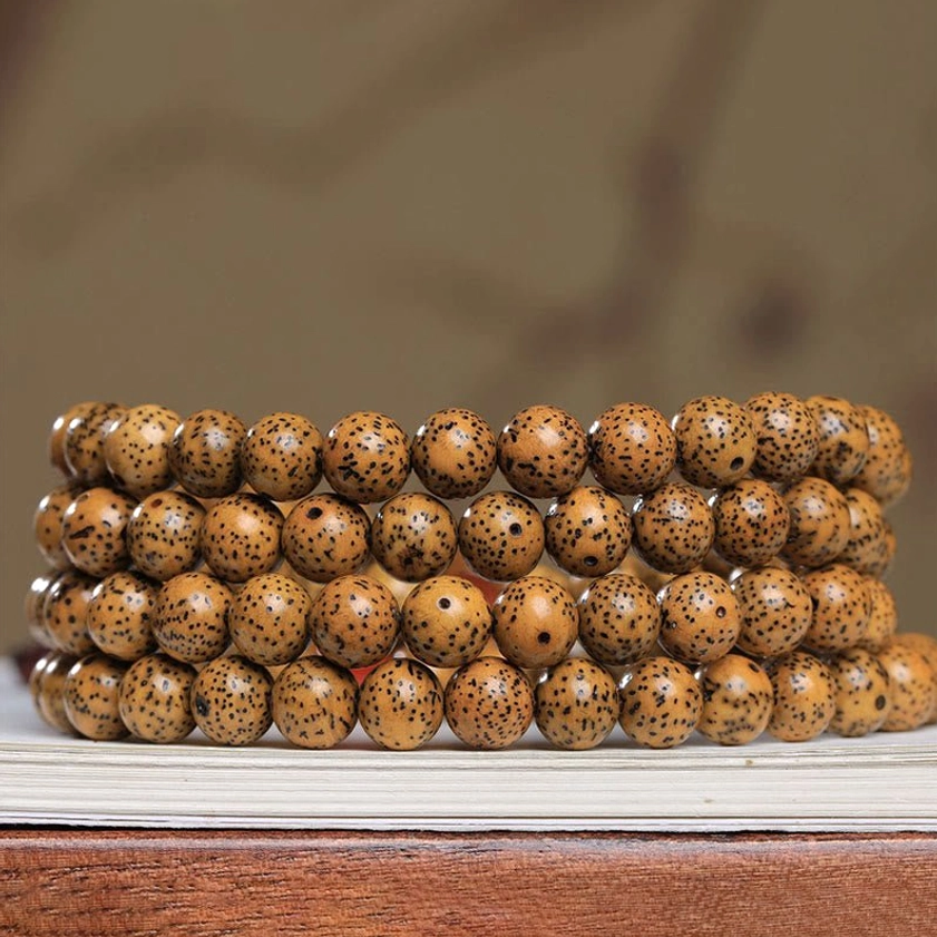 Multiple stacked bodhi seed mala bracelets close-up side view on wooden desk, showing neatly arranged spotted brown bodhi seeds and Buddhist prayer bead details