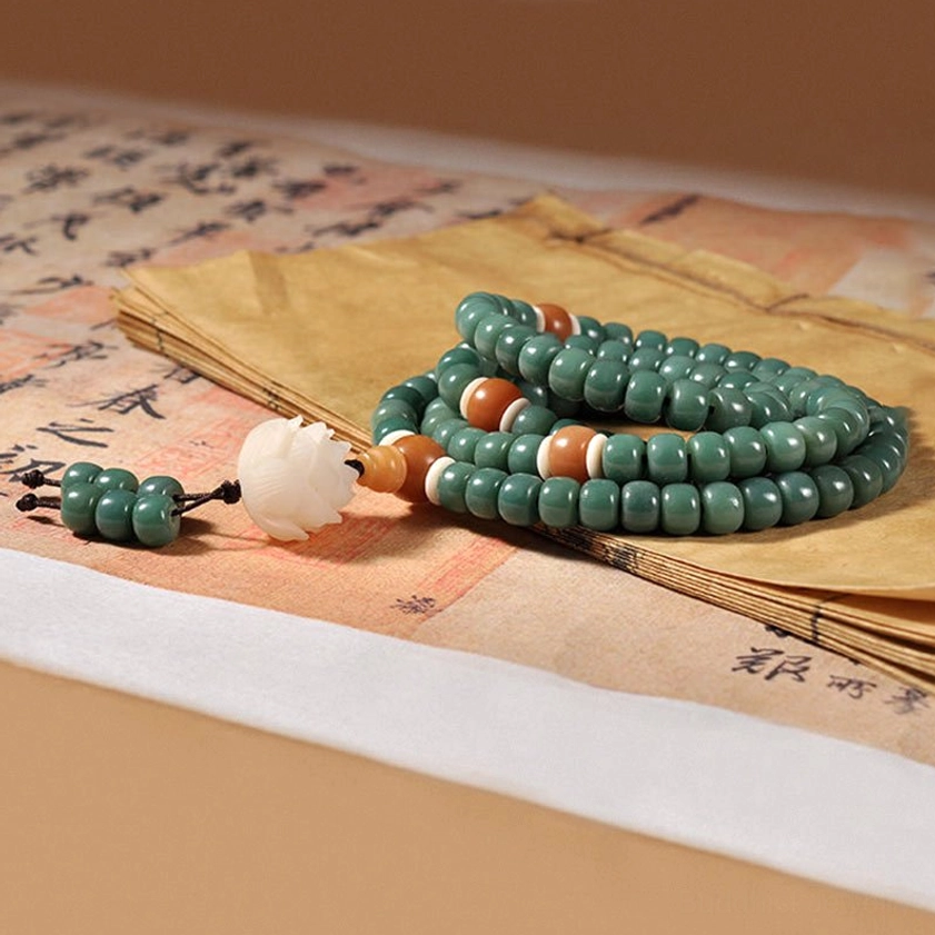 Coiled bodhi seed mala bracelet with green beads, lotus pendant, and tassel on ancient calligraphy paper