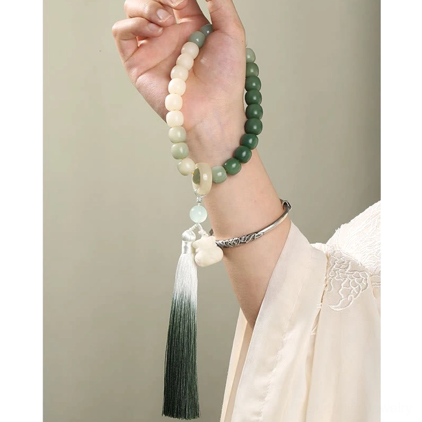Hand holding handmade bodhi seed prayer mala bracelet with gradient green beads, dark ombre tassel, and lotus pendant - first-person perspective of Buddhist meditation bracelet