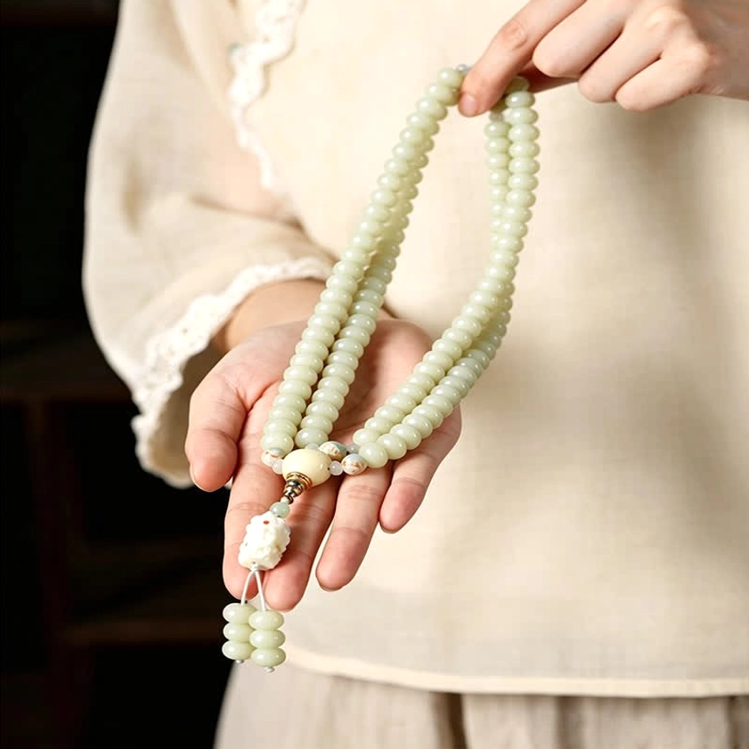 Close-up hands holding white bodhi seed 108 prayer mala with Tara pendant on dark wooden background