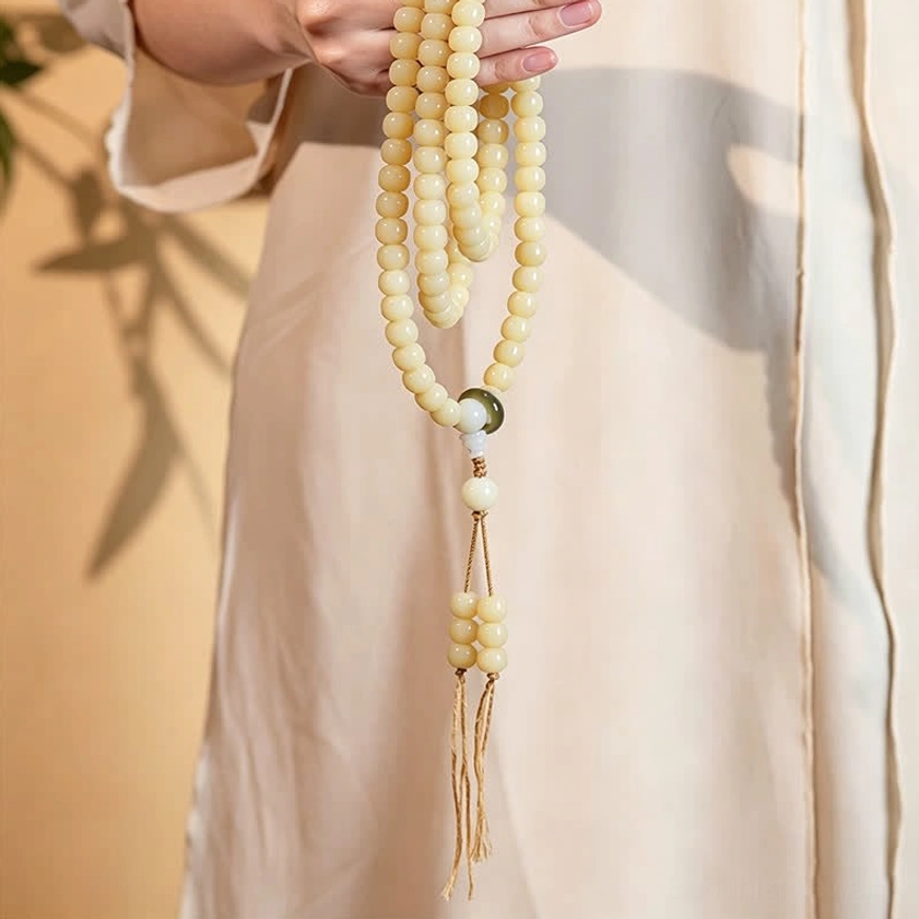 Long bodhi seed mala bracelet draped with lotus pendant and green accent bead, indoor lifestyle setting