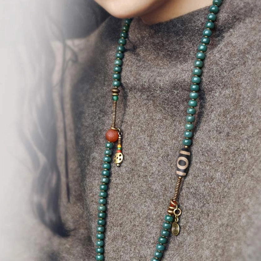 Single-strand 108 mala bead necklace with brass charms and red accent bead worn over grey knit fabric