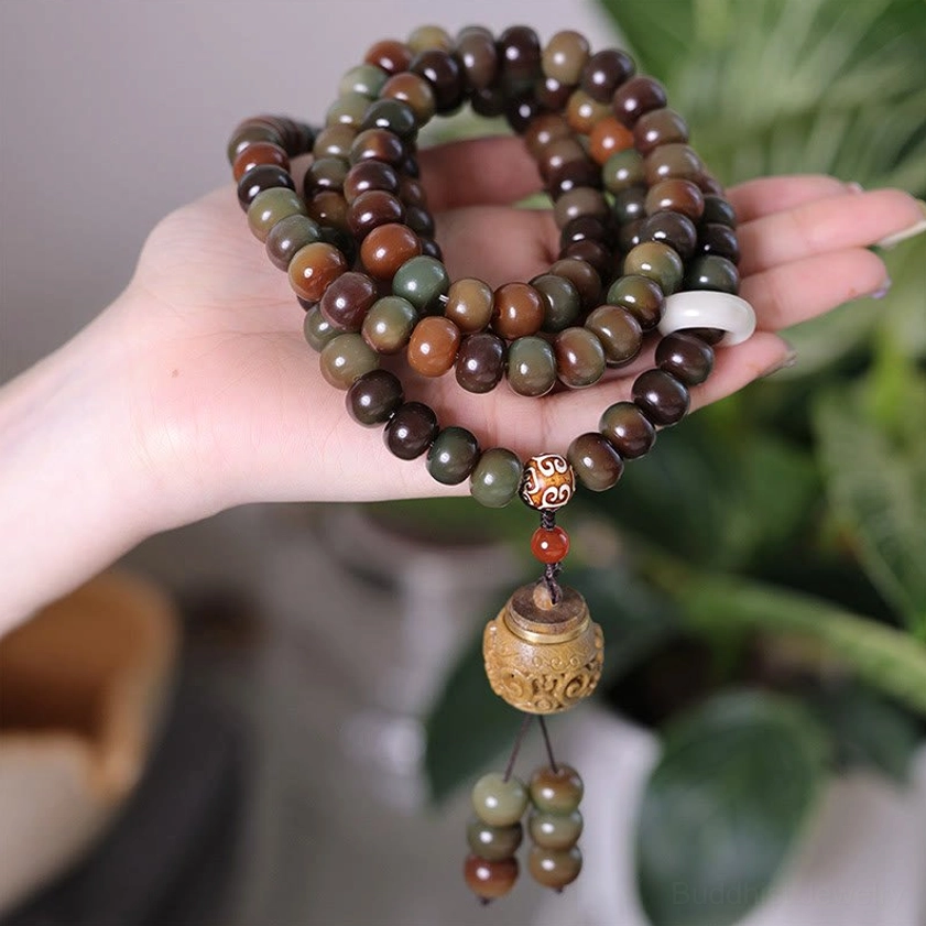 108 Bodhi seed mala prayer beads bracelet with dzi bead and wooden pendant, held in hand with natural green plant background, close-up view