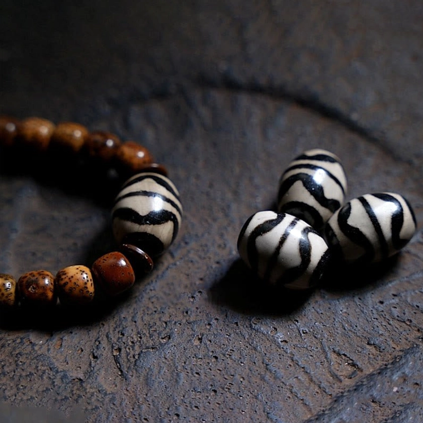 Partial bodhi seed mala bracelet with three black-and-white striped dzi agate beads displayed on dark stone surface