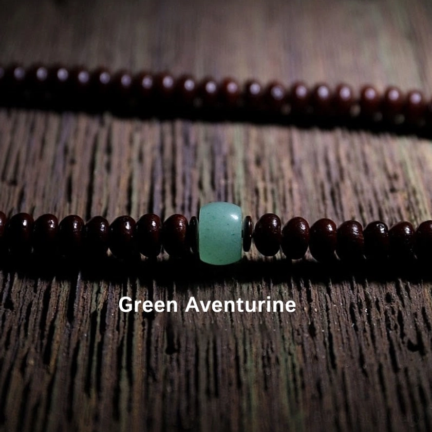Purple bodhi seed mala strand with green aventurine accent bead on wooden surface
