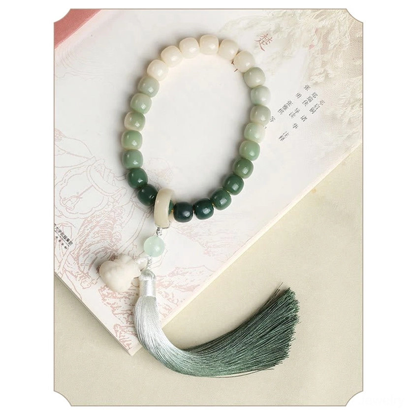 Bodhi seed wrist mala displayed on ancient book with ombre green beads, lotus pendant charm, and two-tone gradient silk tassel - spiritual Buddhist prayer bracelet flat lay