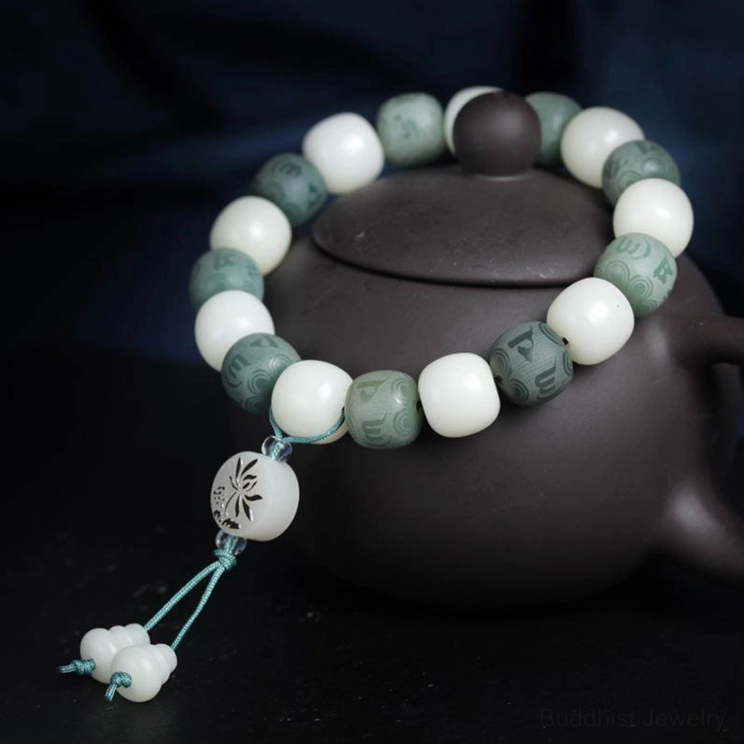 Top-down view of handcrafted white bodhi protection bracelet showing detailed mantra bead carvings and teal cord tassel