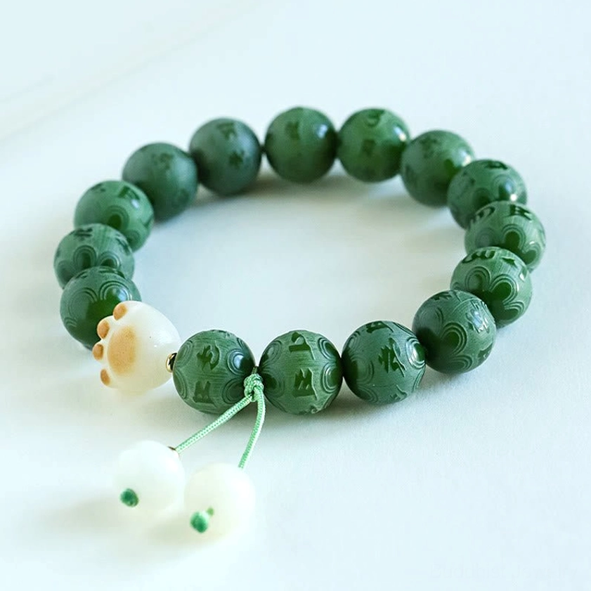 Overhead view of carved Bodhi Seed Buddhist bracelet featuring dark green mantra beads, jade paw-print accent, and white pendants