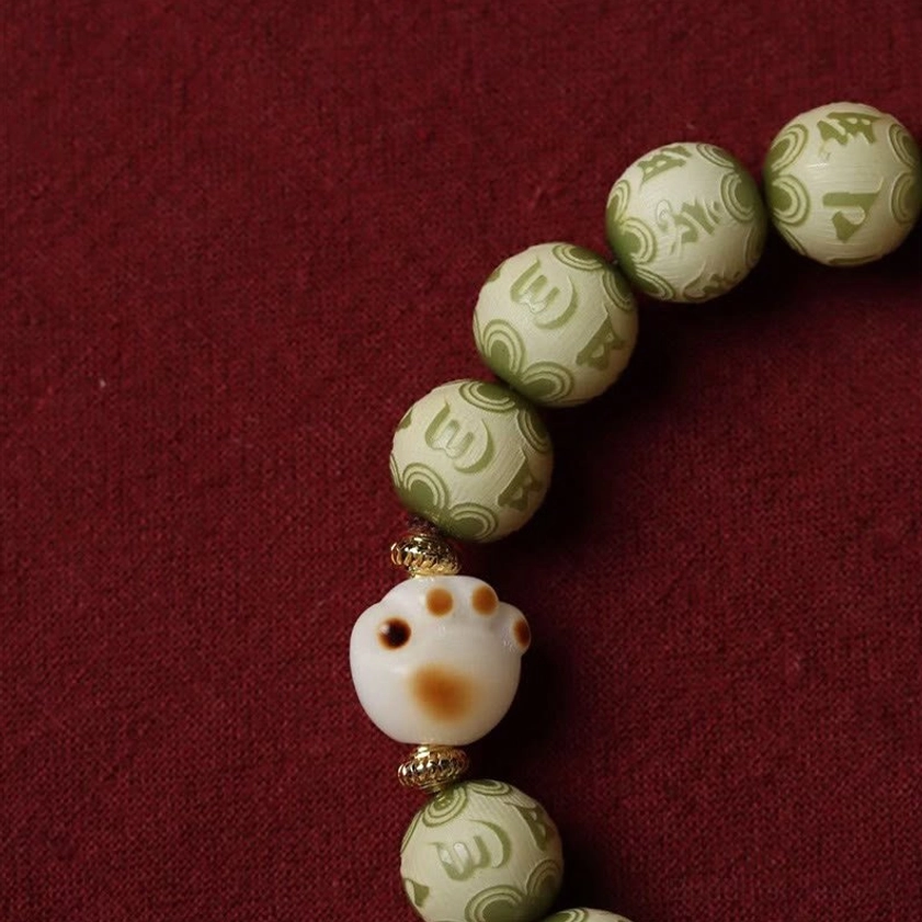 Detailed close-up of green Bodhi seed beads showing engraved Om Mani Padme Hum mantra with white cat paw decoration