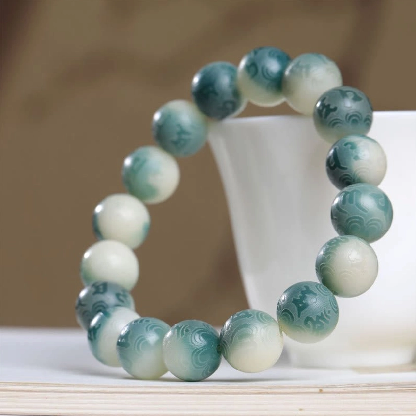 Reverse gradient Bodhi seed prayer bracelet with jade spacer ring shown on white cup and vintage book