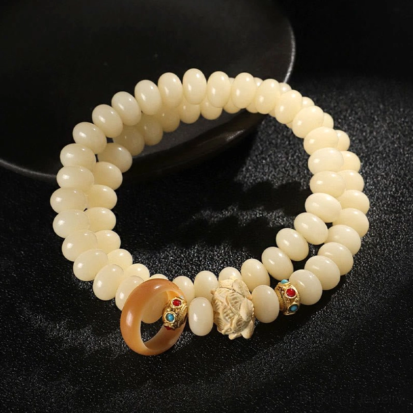 Double wrap bodhi seed and peach wood lotus bracelet displayed flat lay - handmade Buddhist bracelet with cream beads and wooden lotus charm