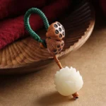 White bodhi seed peach wood lotus keychain with braided green rope and carved lotus pendant on wooden tray