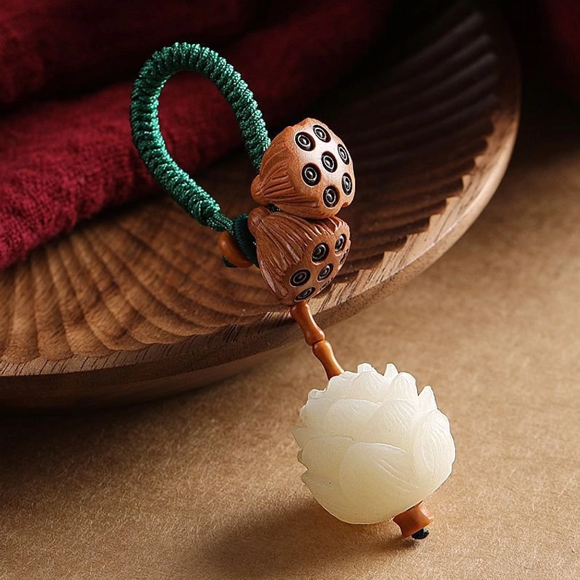 White bodhi seed peach wood lotus keychain with braided green rope and carved lotus pendant on wooden tray