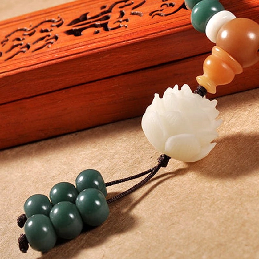 Overhead close-up of smooth barrel bodhi seeds with lotus pendant and bead tassel in carved wooden box