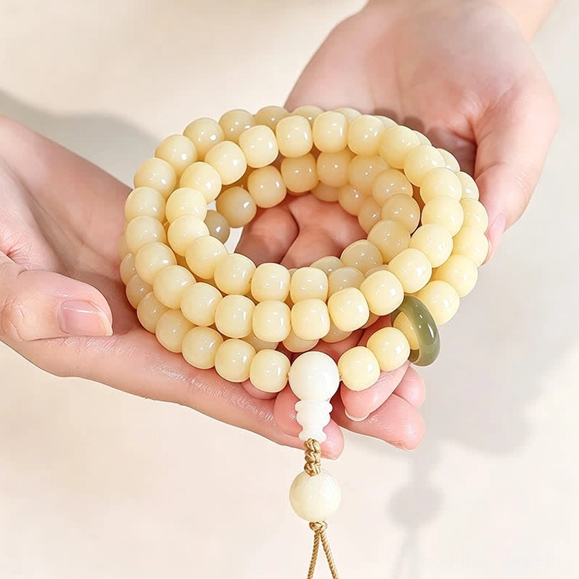 Close-up of hand-polished bodhi seed beads held in palms, showing smooth ivory finish and green jade ring accent