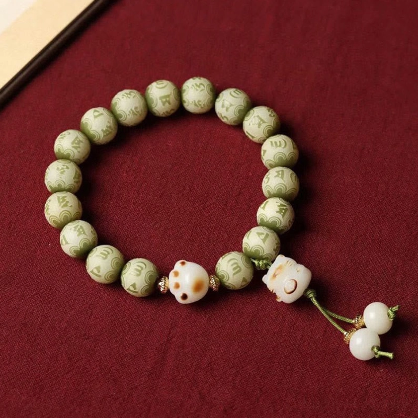 Close-up overhead view of green Bodhi seed prayer bracelet featuring engraved mantra beads and cat paw charm details