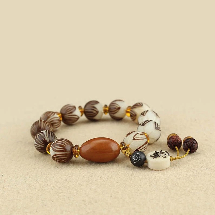 Overhead view of bodhi seed prayer bracelet with brown-white patterned beads and brown oval focal bead on light background