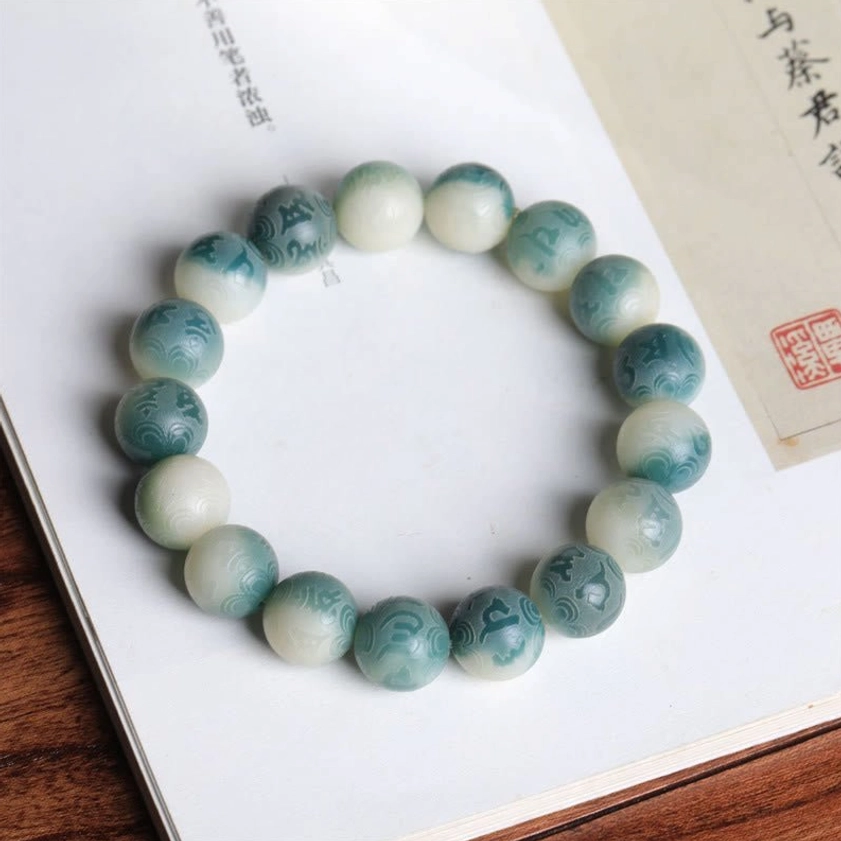Round carved Bodhi seed prayer bracelet with Om Mani Padme Hum mantra and jade ring on book display