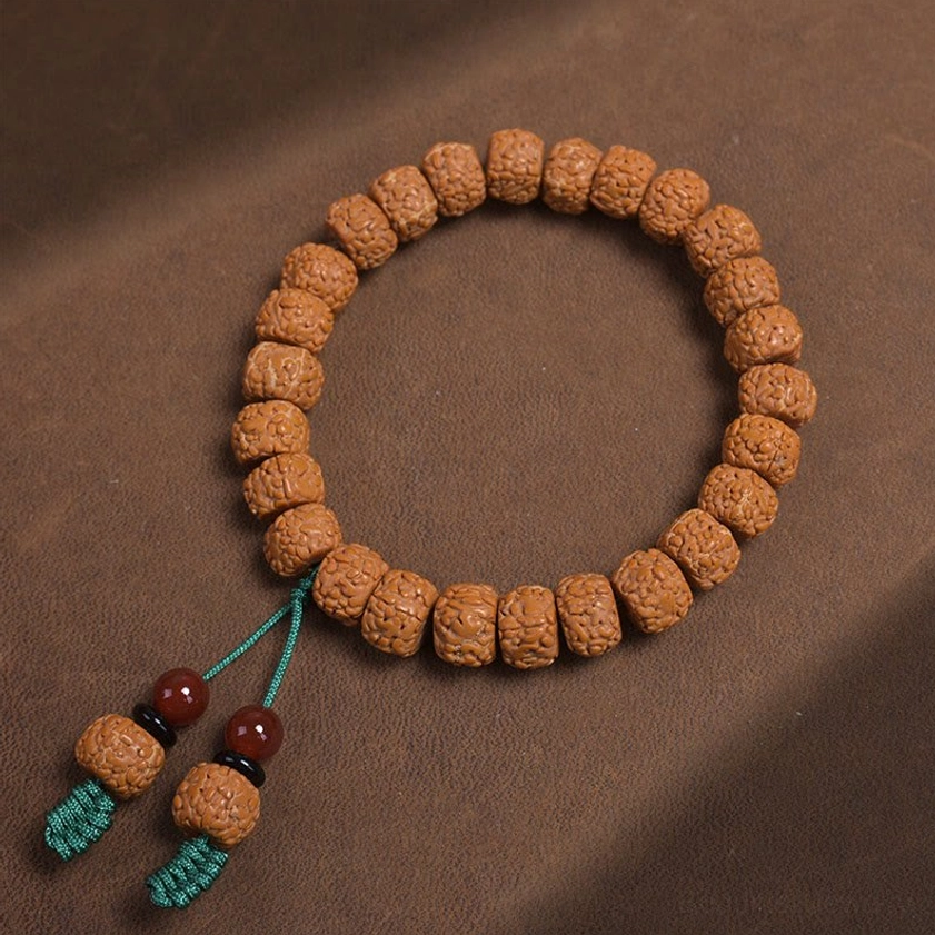 Buddhist prayer bracelet flat lay showing brown textured beads with green tassel and red agate accents