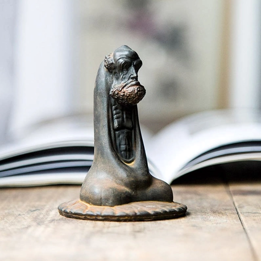 Bodhidharma home decor statue three-quarter view on table with book and lotus-shaped base