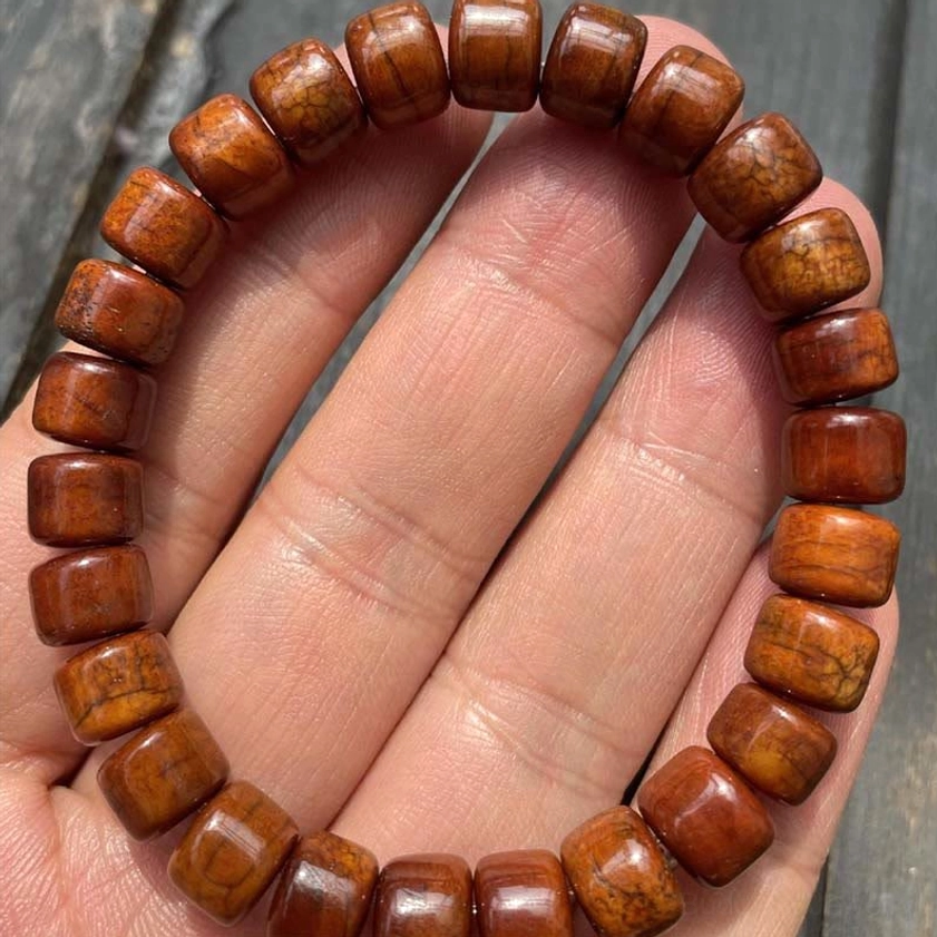 Bone bead bracelet close-up on palm showing polished cylindrical beads and natural grain