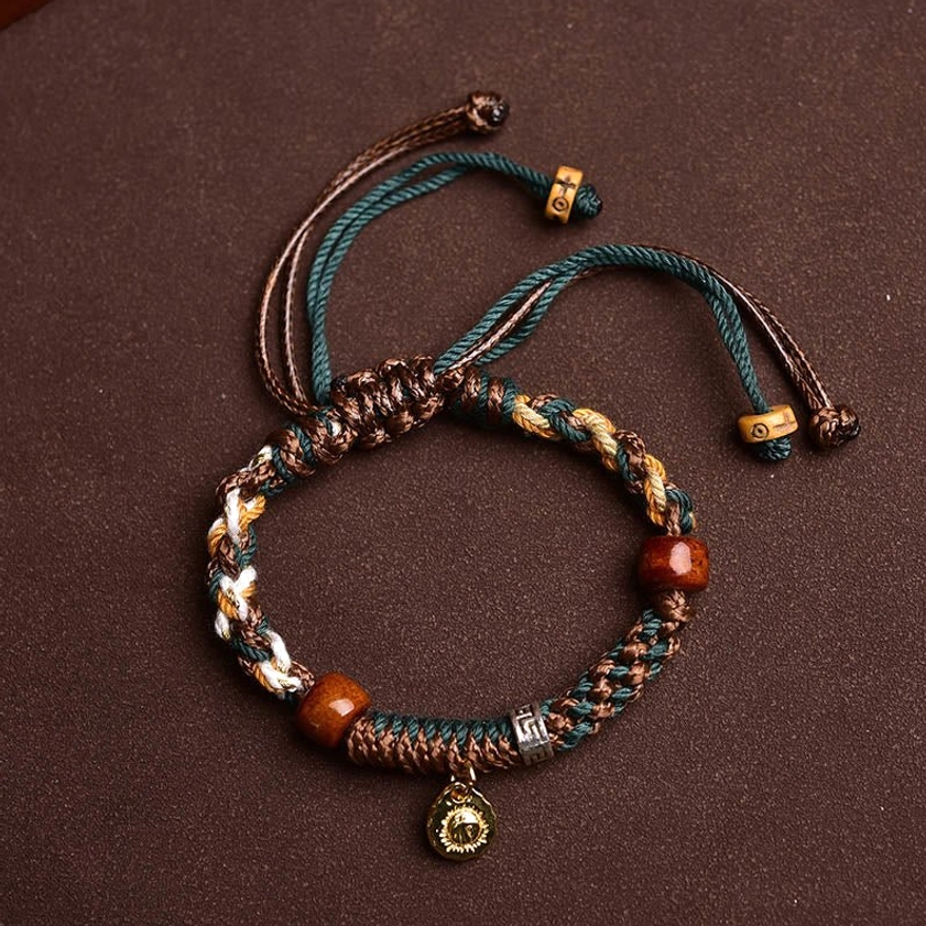 Buddhist protection bracelet with mixed brown white green braided rope, natural bone beads, and hanging metal pendant - flat lay view