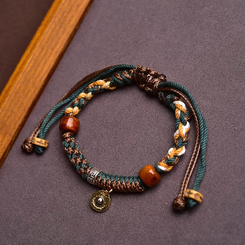 Handmade Buddhist protection bracelet with multicolor braided rope, natural bone beads, and metal pendant - high angle view