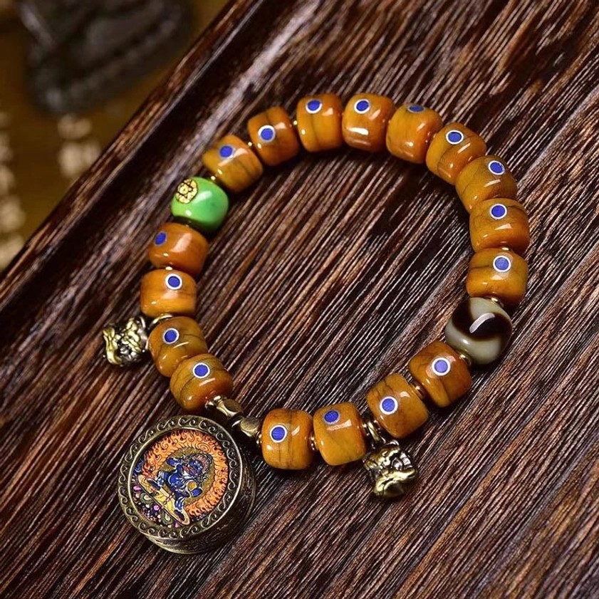 Handcrafted bone bead Buddhist bracelet with lazurite stones and copper bell pendant, overhead view on wooden desk