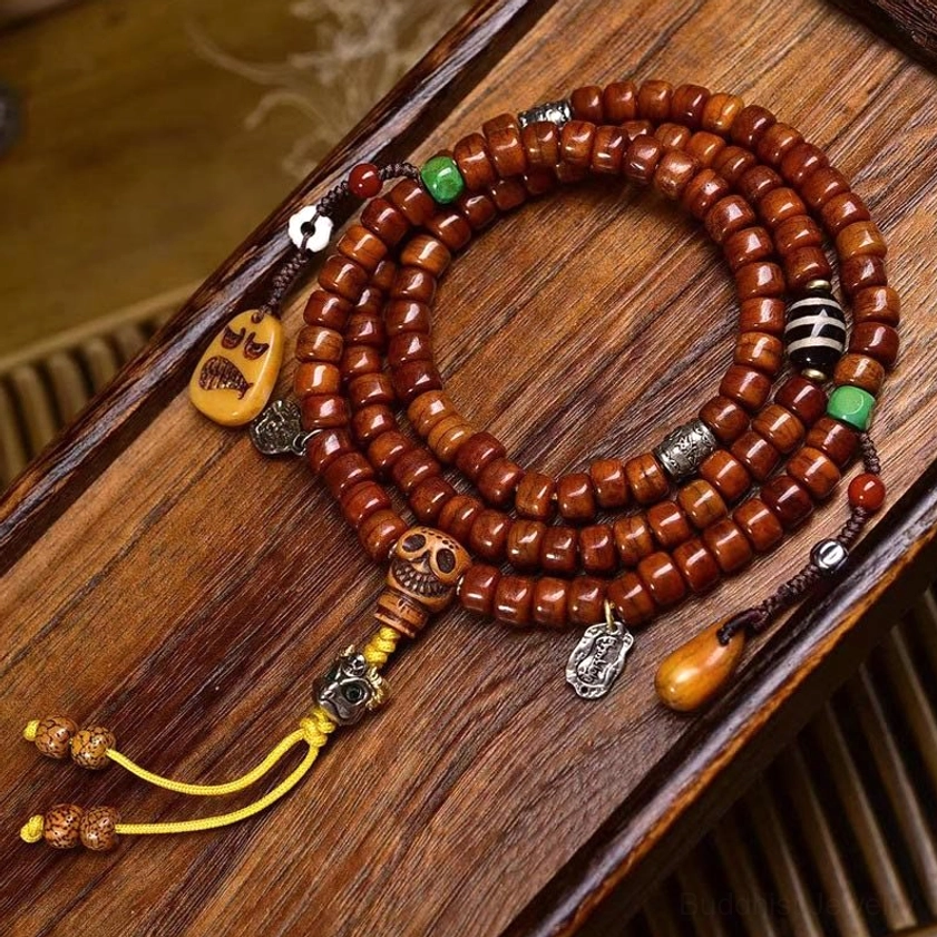 108 bone bead Buddhist prayer mala bracelet with hand-painted Dzi amulet, skull guru bead, copper pendants and yellow tassel laid flat on wooden surface