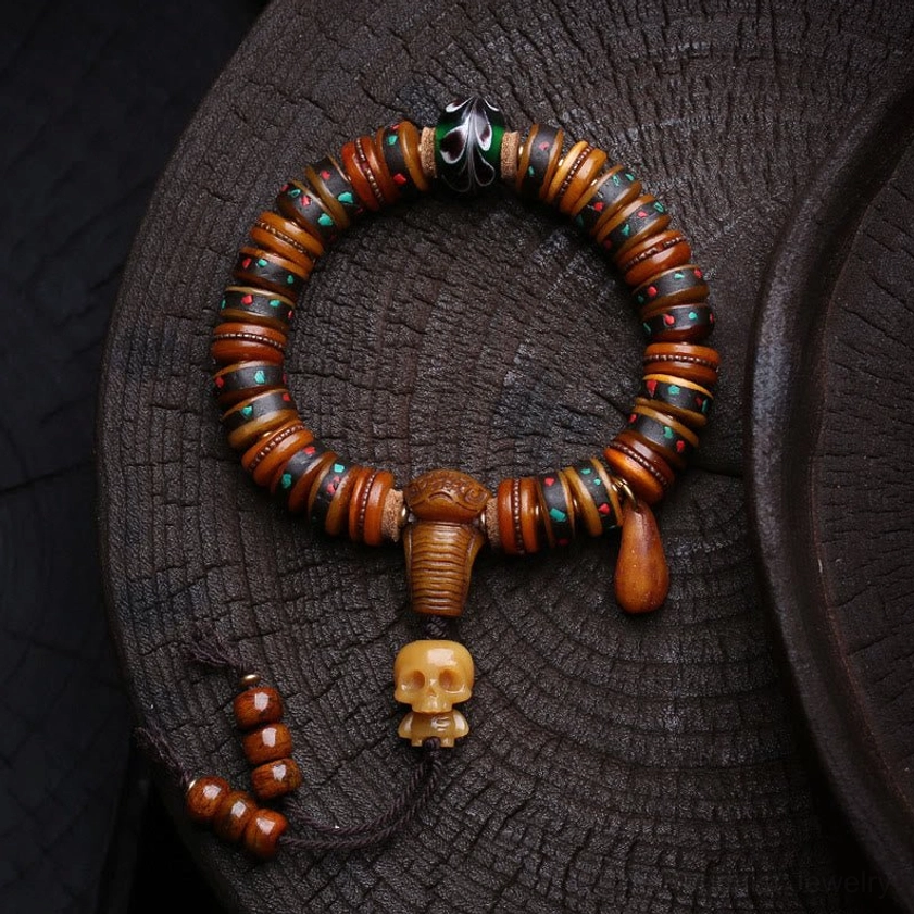 Handcrafted bone bead skull bracelet with carved bone beads and resin skull pendant on wooden tray, Buddhist protection bracelet