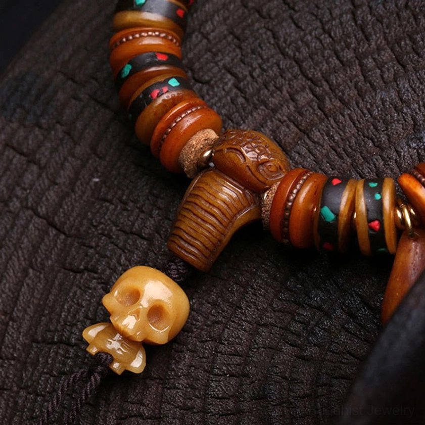 Close-up of bone bead bracelet terminal charms with carved skull pendant and inlaid spacers, handmade Buddhist bracelet