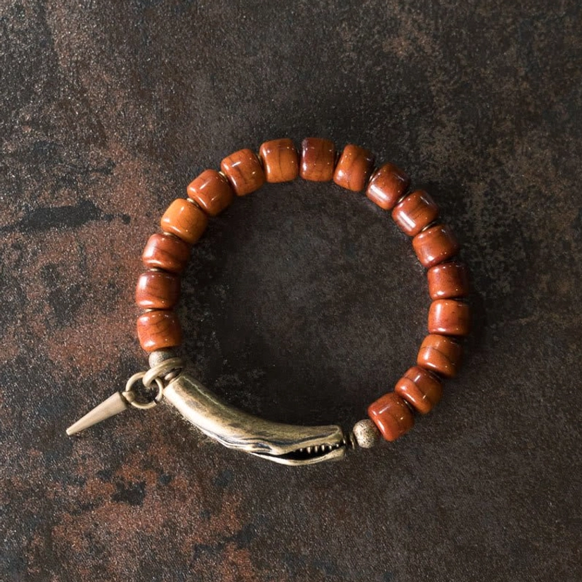 Natural bone beads stretch bracelet in full flat lay showing cylindrical brown beads, bronze metal clasp, and pointed spike accent on dark brown background