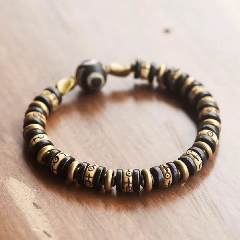 Flat lay top view of ebony wood Buddhist bracelet on wooden surface, displaying stacked disc beads and engraved symbols with Dzi bead