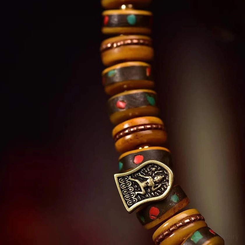 Close-up of camel bone bracelet beads with red-green inlaid details and metal Buddha-themed charm accent