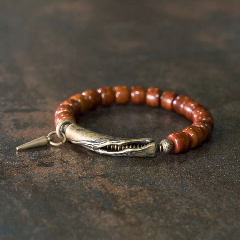 Handcrafted bone beads copper cone pendant strength bracelet displayed overhead on dark rustic metal background, showing brown cylinder beads with antique bronze clasp and spike charm